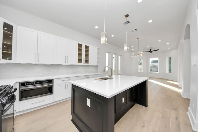 kitchen featuring ceiling fan, stainless steel oven, a kitchen island with sink, hanging light fixtures, and black range with gas cooktop