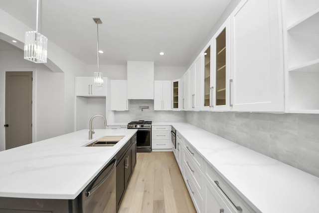 kitchen featuring sink, white cabinetry, hanging light fixtures, appliances with stainless steel finishes, and an island with sink