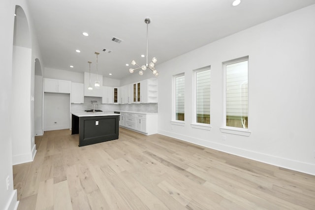 kitchen with decorative light fixtures, tasteful backsplash, a center island with sink, sink, and white cabinetry