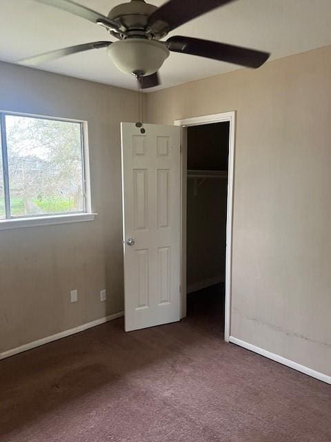 unfurnished bedroom featuring dark carpet, a spacious closet, ceiling fan, and a closet