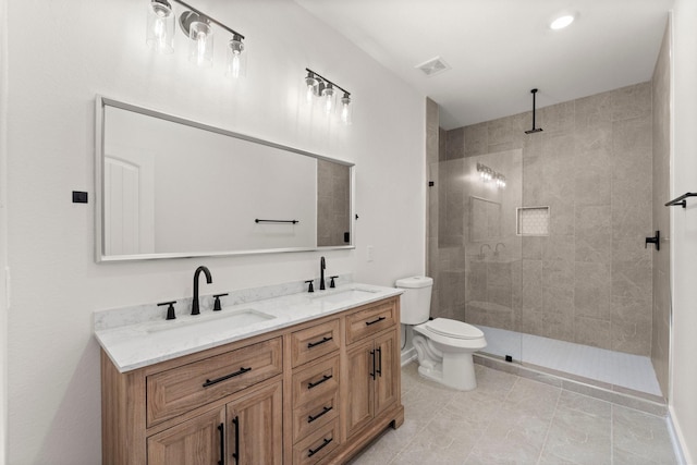 bathroom with toilet, vanity, a tile shower, and tile patterned flooring