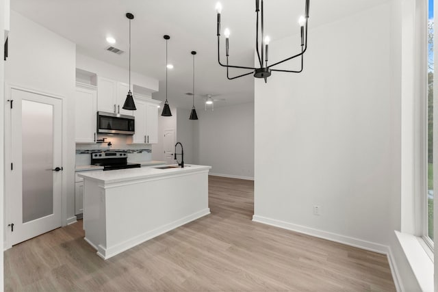 kitchen featuring decorative light fixtures, white cabinetry, stainless steel appliances, an island with sink, and sink