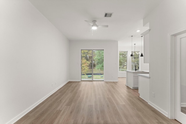 unfurnished living room featuring ceiling fan with notable chandelier, sink, and light wood-type flooring