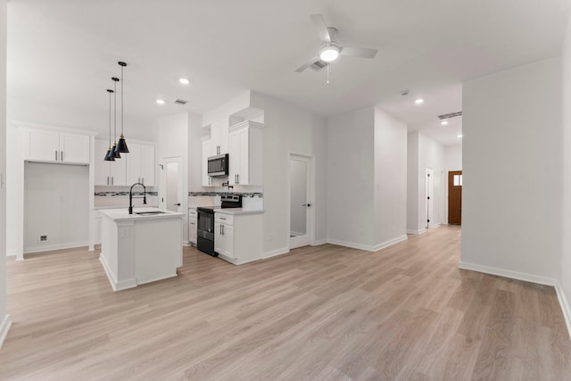 kitchen featuring white cabinetry, pendant lighting, a center island with sink, and stove