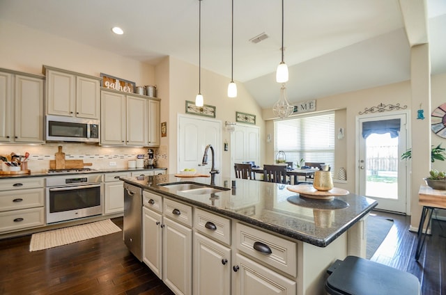 kitchen with appliances with stainless steel finishes, lofted ceiling, sink, hanging light fixtures, and a kitchen island with sink