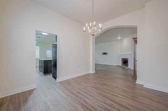 unfurnished dining area with a fireplace, a chandelier, and light hardwood / wood-style flooring