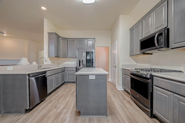 kitchen featuring a kitchen island, appliances with stainless steel finishes, sink, gray cabinetry, and a textured ceiling