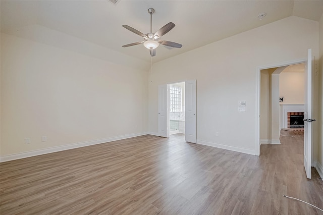 empty room featuring ceiling fan, vaulted ceiling, a fireplace, and light hardwood / wood-style floors