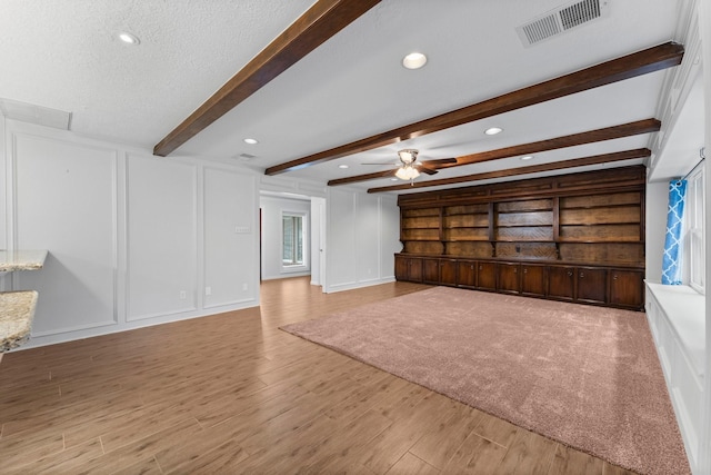 unfurnished living room with plenty of natural light, a textured ceiling, beam ceiling, and light hardwood / wood-style floors