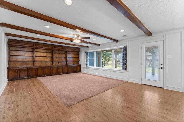 unfurnished living room featuring beamed ceiling, ceiling fan, a textured ceiling, and light hardwood / wood-style flooring