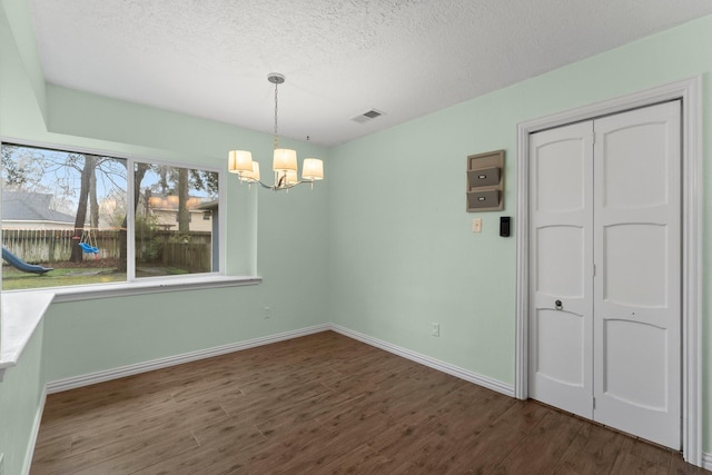 unfurnished dining area with dark hardwood / wood-style floors, a textured ceiling, and a chandelier