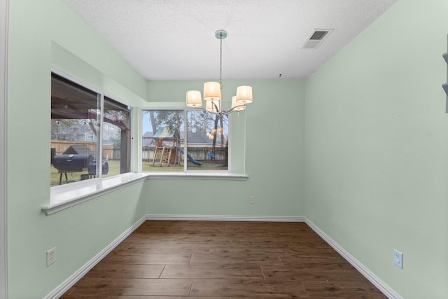 unfurnished dining area with an inviting chandelier, dark hardwood / wood-style flooring, and a textured ceiling