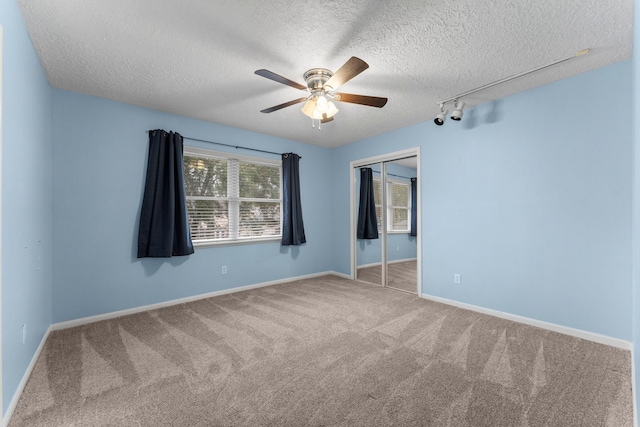 carpeted empty room with ceiling fan, track lighting, and a textured ceiling