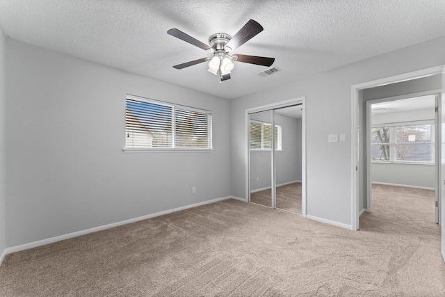 unfurnished bedroom with multiple windows, light colored carpet, a closet, and a textured ceiling