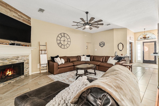 tiled living room featuring ceiling fan with notable chandelier, a textured ceiling, and a stone fireplace