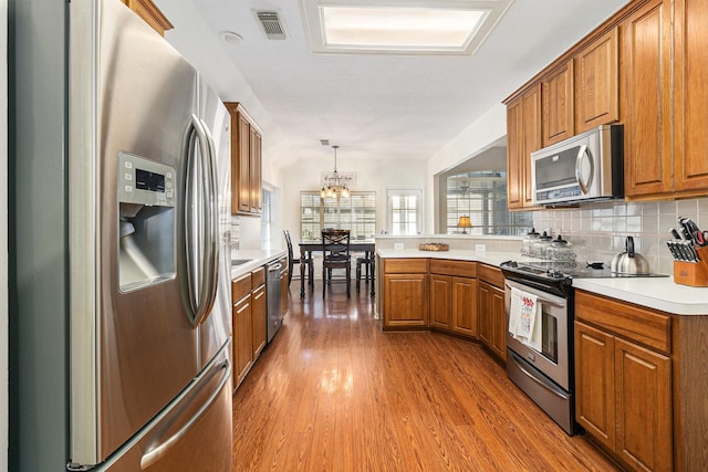 kitchen featuring hardwood / wood-style floors, tasteful backsplash, a chandelier, pendant lighting, and stainless steel appliances