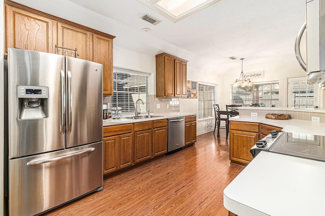 kitchen with a notable chandelier, wood-type flooring, hanging light fixtures, sink, and stainless steel appliances