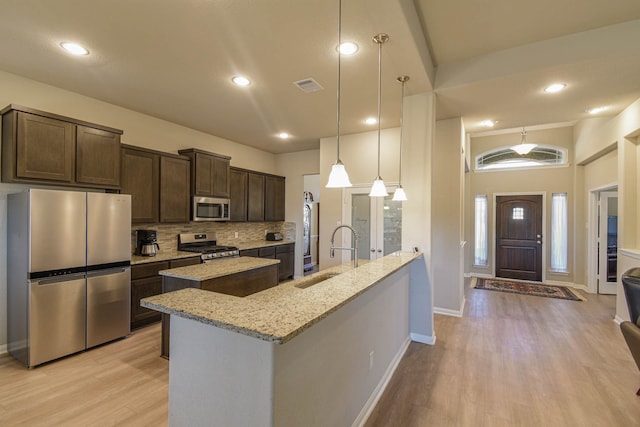 kitchen featuring sink, dark brown cabinets, appliances with stainless steel finishes, pendant lighting, and light stone countertops