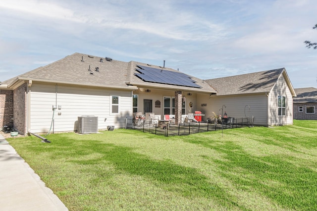 back of property featuring cooling unit, a lawn, and solar panels