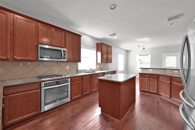 kitchen featuring appliances with stainless steel finishes, a kitchen island, decorative light fixtures, backsplash, and dark hardwood / wood-style floors