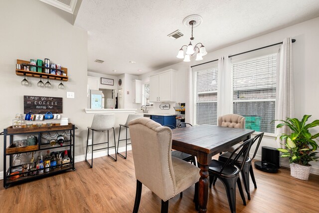 dining area featuring light hardwood / wood-style floors, sink, a textured ceiling, and a notable chandelier