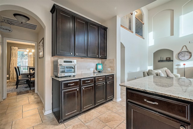 kitchen with light stone counters, light tile patterned floors, backsplash, and dark brown cabinetry