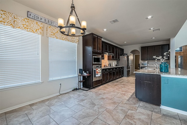 kitchen featuring decorative light fixtures, sink, light stone counters, stainless steel appliances, and dark brown cabinets