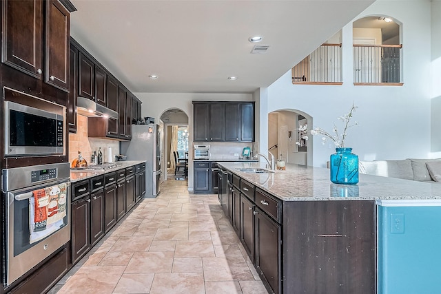 kitchen featuring stainless steel appliances, an island with sink, and dark brown cabinets