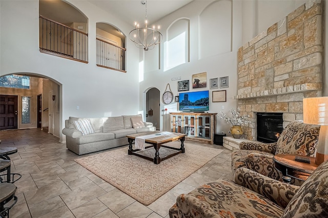 living room with a notable chandelier, a stone fireplace, and a high ceiling