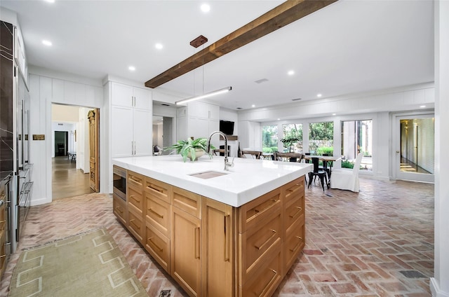 kitchen with a center island with sink, stainless steel microwave, beam ceiling, white cabinets, and sink