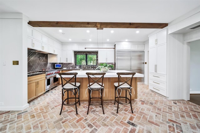 kitchen with a kitchen island, high end appliances, backsplash, beam ceiling, and a breakfast bar area