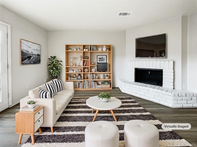 living room featuring a brick fireplace and dark hardwood / wood-style flooring