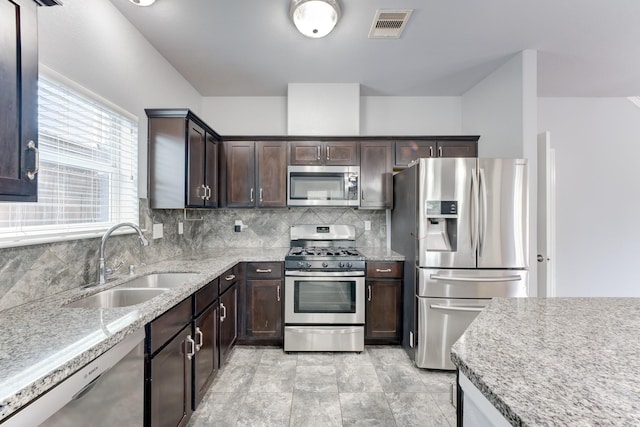 kitchen with backsplash, sink, dark brown cabinetry, light stone countertops, and stainless steel appliances