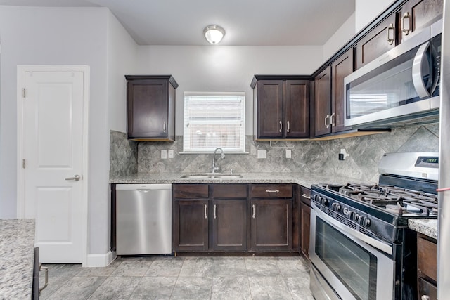 kitchen featuring stainless steel appliances, dark brown cabinets, light stone counters, and sink