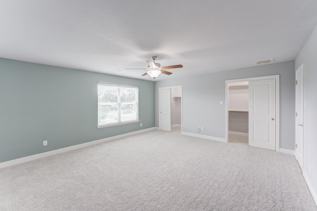 unfurnished bedroom featuring ceiling fan, light colored carpet, a closet, and a walk in closet