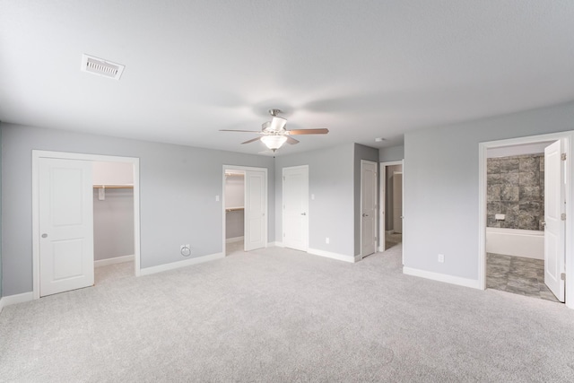 unfurnished bedroom with light carpet, ensuite bathroom, ceiling fan, a closet, and a walk in closet