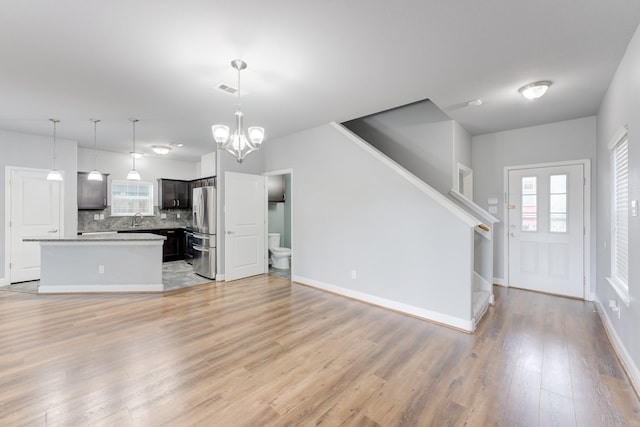 unfurnished living room with sink, an inviting chandelier, and light hardwood / wood-style flooring