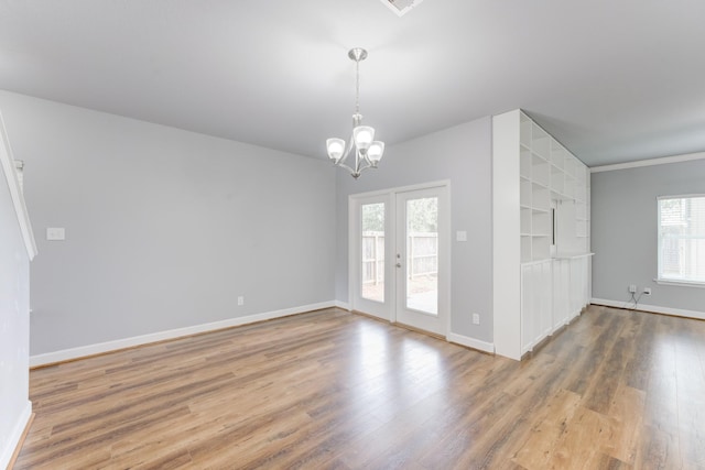 spare room featuring wood-type flooring, plenty of natural light, french doors, and a notable chandelier