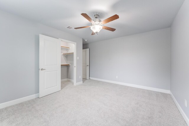 unfurnished bedroom with ceiling fan, a walk in closet, and light carpet