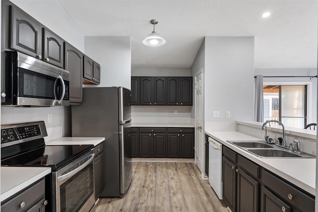 kitchen with appliances with stainless steel finishes, sink, light hardwood / wood-style flooring, and decorative light fixtures