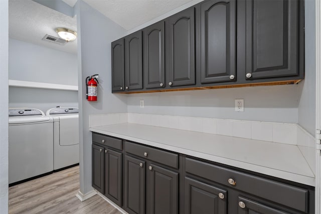 clothes washing area with light hardwood / wood-style flooring, washing machine and dryer, and a textured ceiling