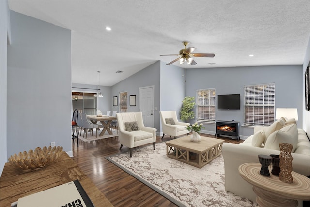 living room with vaulted ceiling, ceiling fan with notable chandelier, a fireplace, wood-type flooring, and a textured ceiling