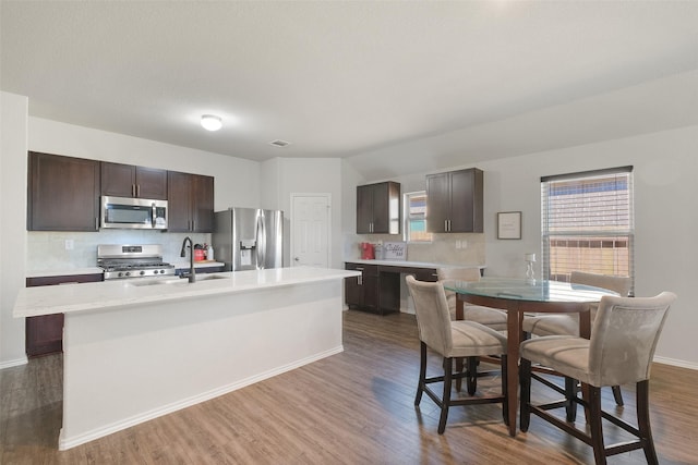 kitchen with decorative backsplash, an island with sink, stainless steel appliances, and dark brown cabinetry