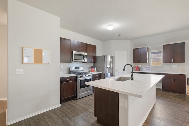 kitchen with appliances with stainless steel finishes, sink, dark brown cabinets, and an island with sink