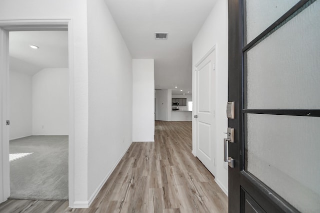 hall featuring light wood-style flooring, visible vents, and baseboards