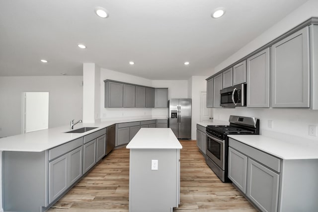 kitchen featuring appliances with stainless steel finishes, a center island, a sink, and gray cabinetry