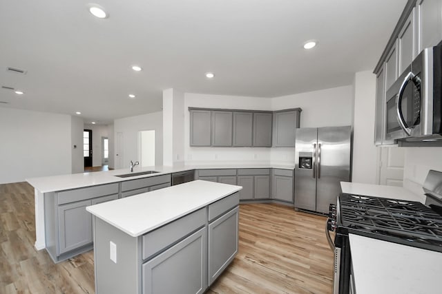 kitchen with a peninsula, stainless steel appliances, gray cabinets, light countertops, and a sink