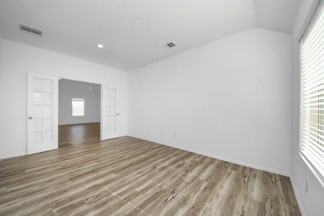 empty room with light wood-style floors, a wealth of natural light, visible vents, and lofted ceiling