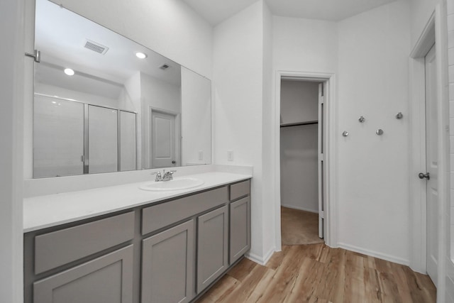 bathroom featuring visible vents, wood finished floors, a walk in closet, vanity, and a shower stall