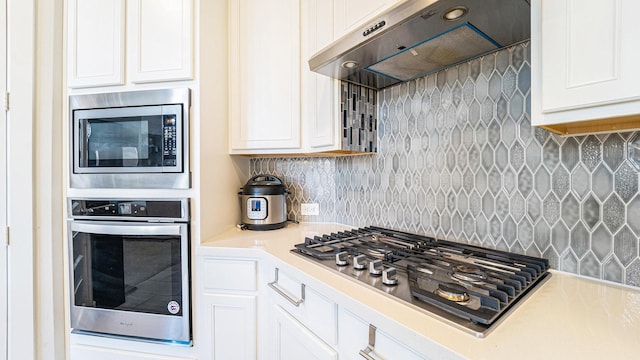 kitchen with decorative backsplash, appliances with stainless steel finishes, wall chimney range hood, and white cabinetry